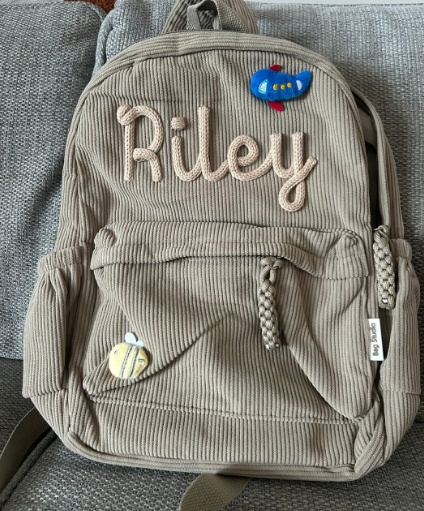 Beige corduroy backpack embroidered 'Riley' with plane and bee charms